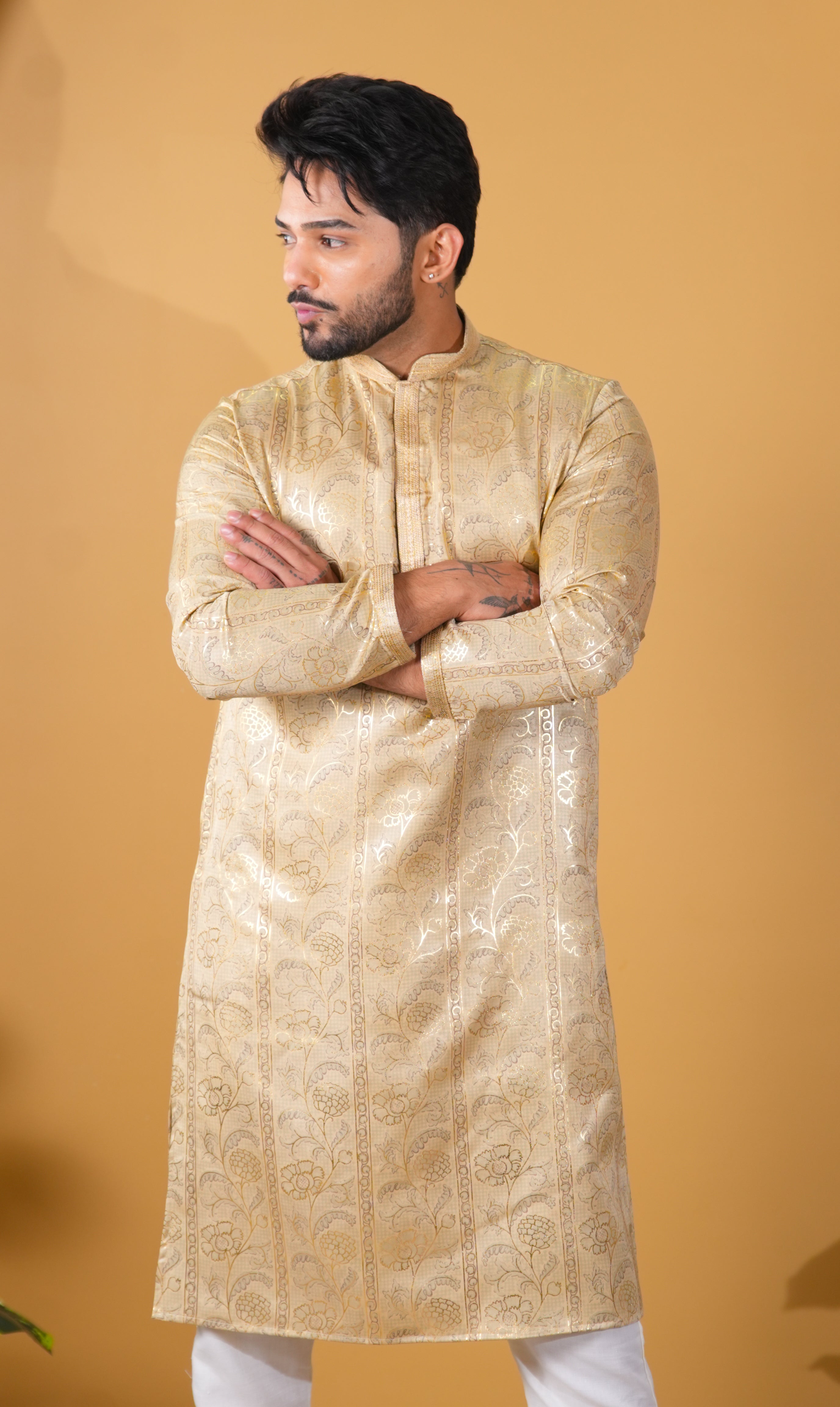 Man wearing a gold kurta with white pants against a beige background