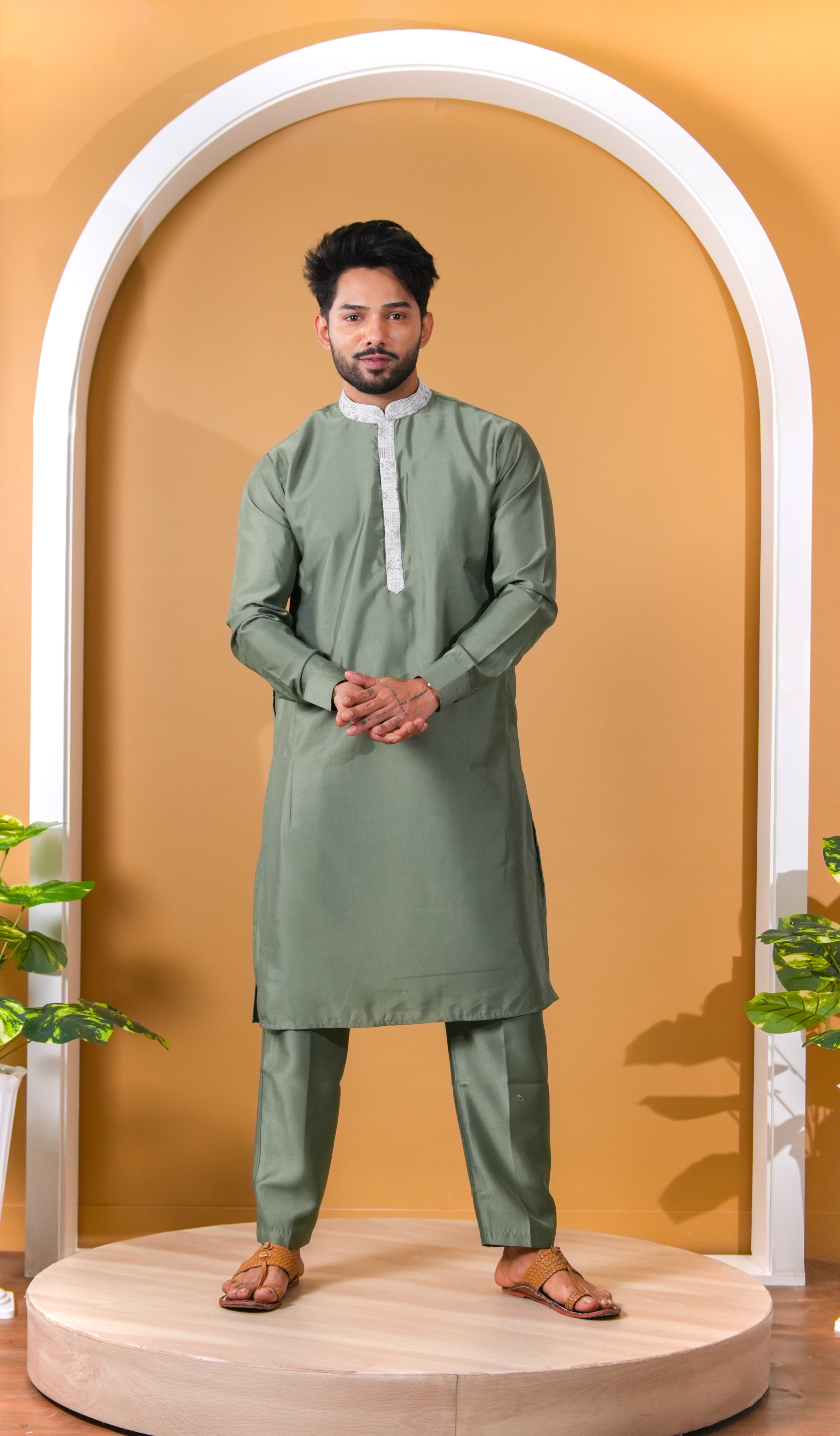 Man wearing a green kurta with white collar against a mustard yellow wall.
