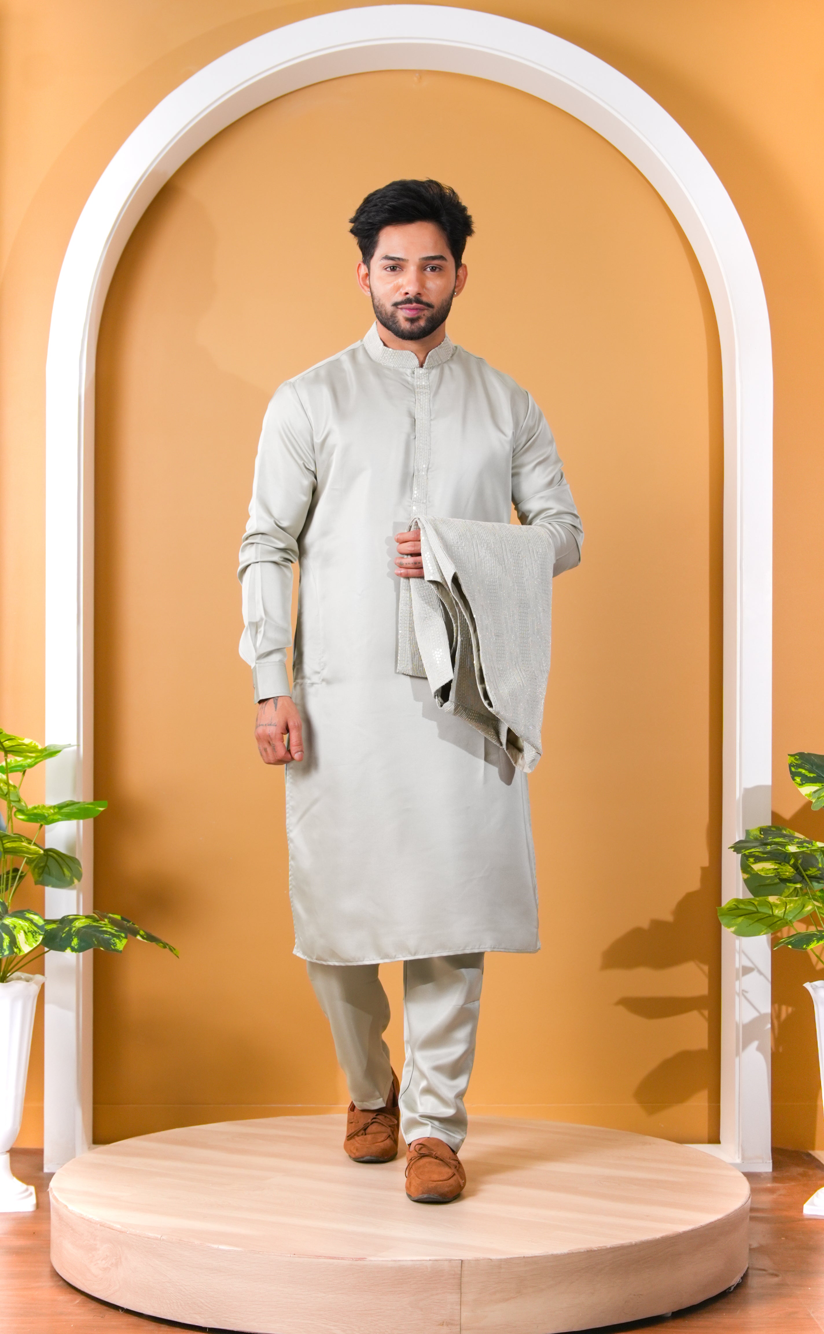 Man wearing a traditional outfit standing in front of an archway with a yellow background