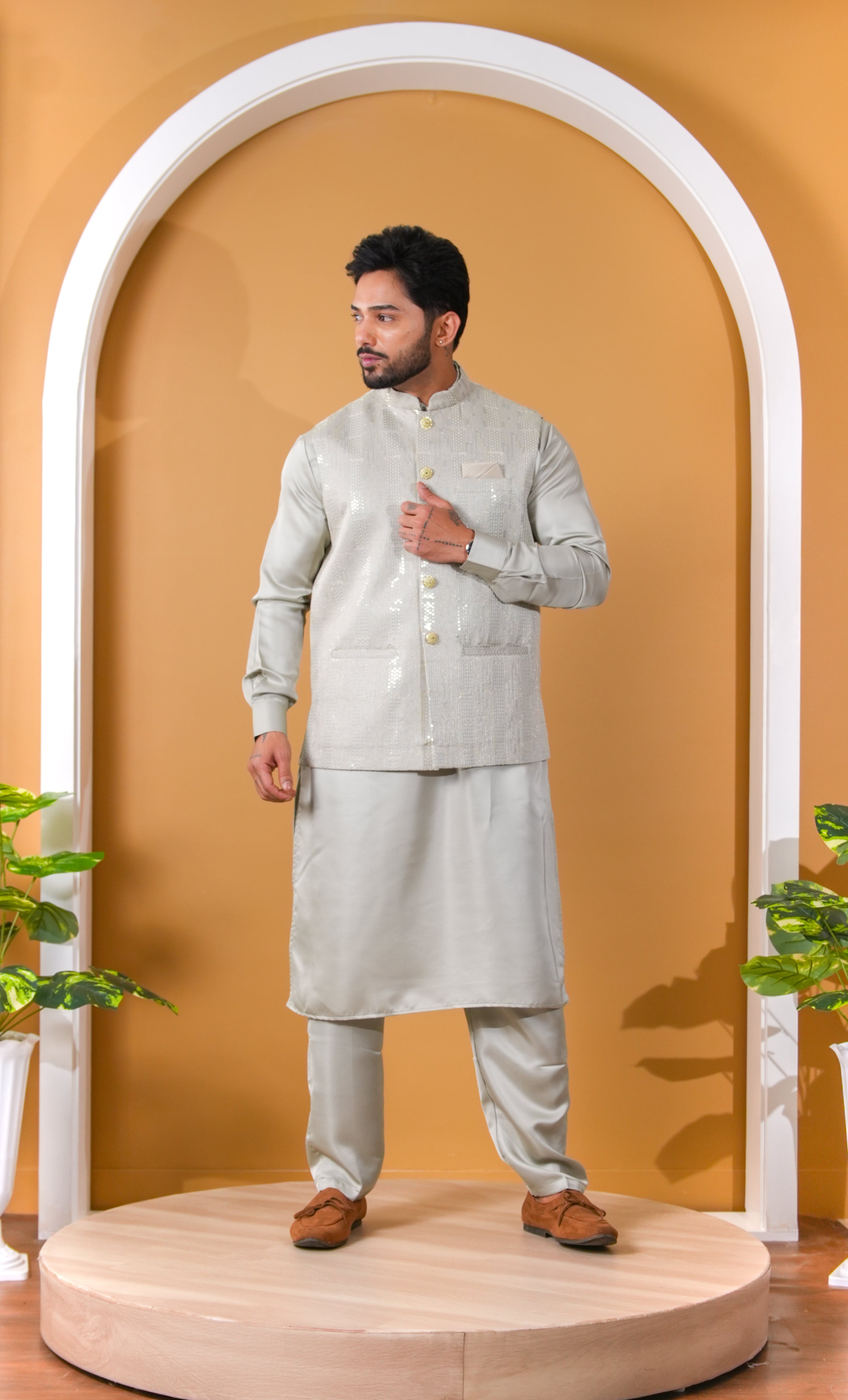 Man wearing a traditional light gray kurta with white pants against a beige background