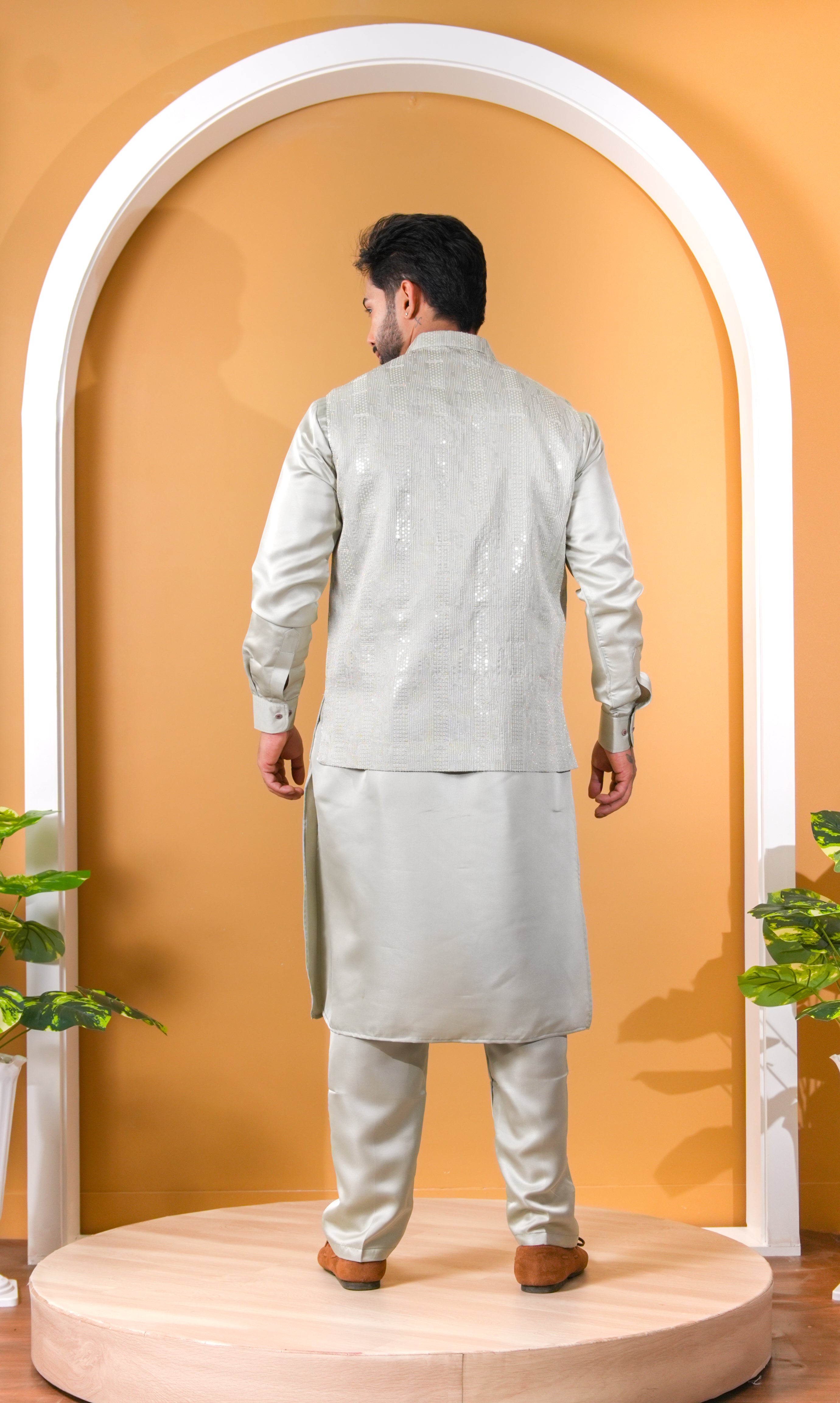 Man wearing a light gray traditional outfit standing in front of an archway with a yellow wall.