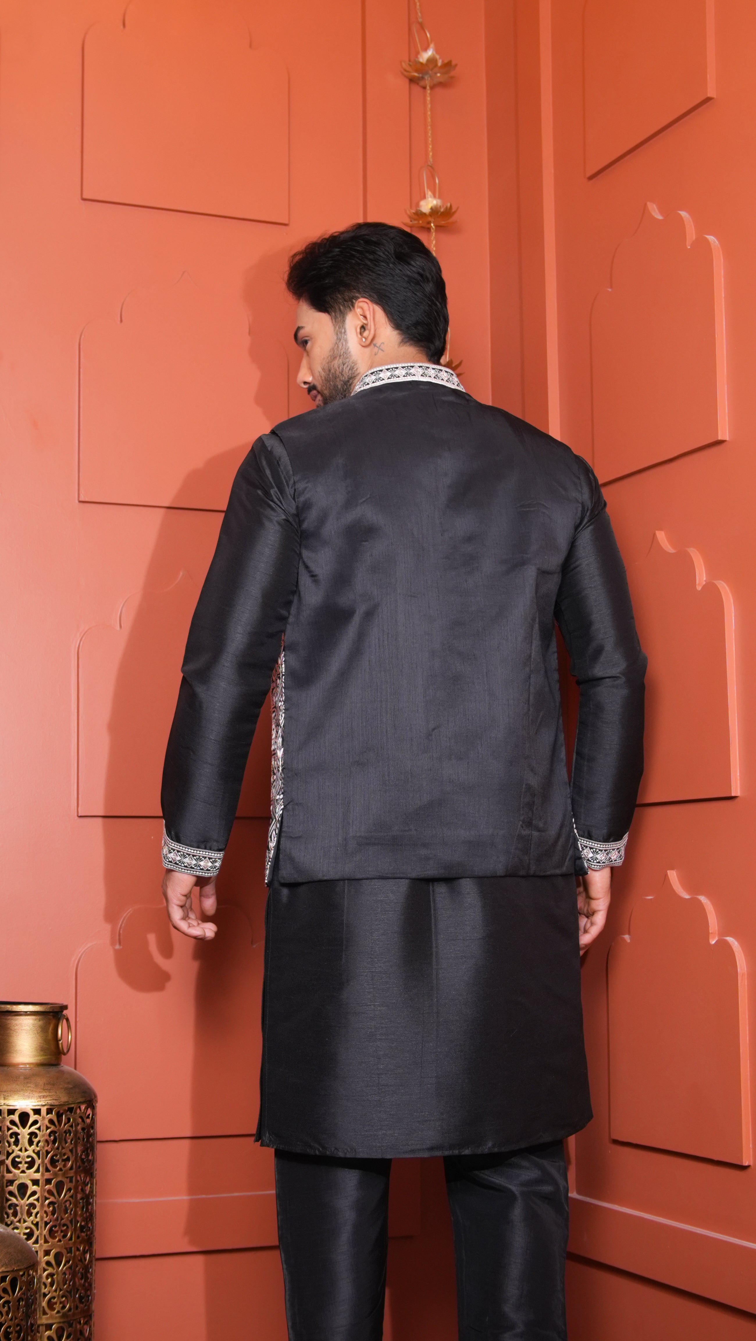 Man wearing a black sherwani against an orange wall.