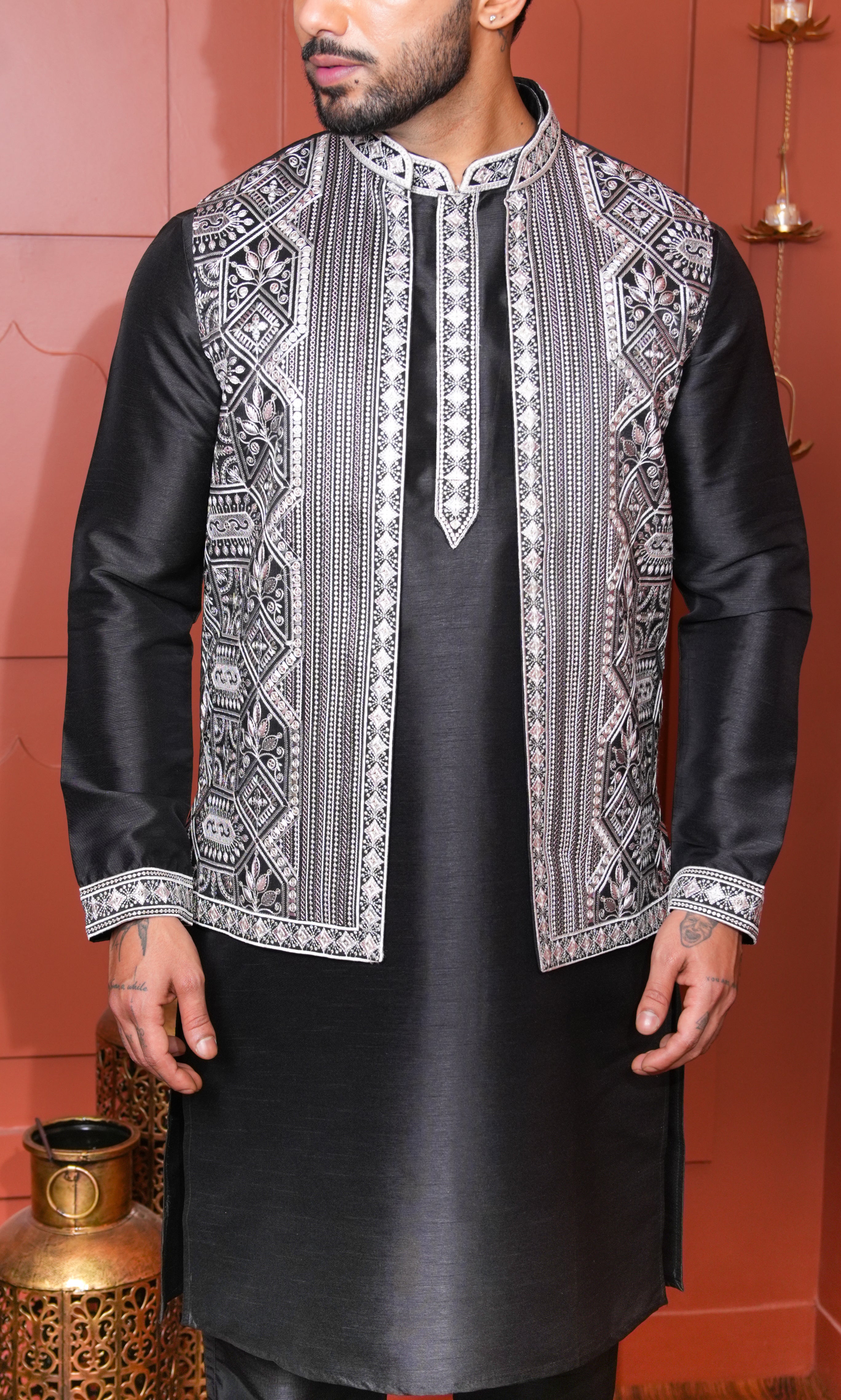 Man wearing a black kurta with white embroidery on a red background
